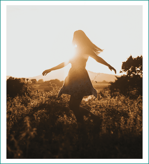 A woman standing in the grass with her arms outstretched.