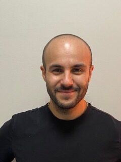 Smiling man in black shirt, neutral background.