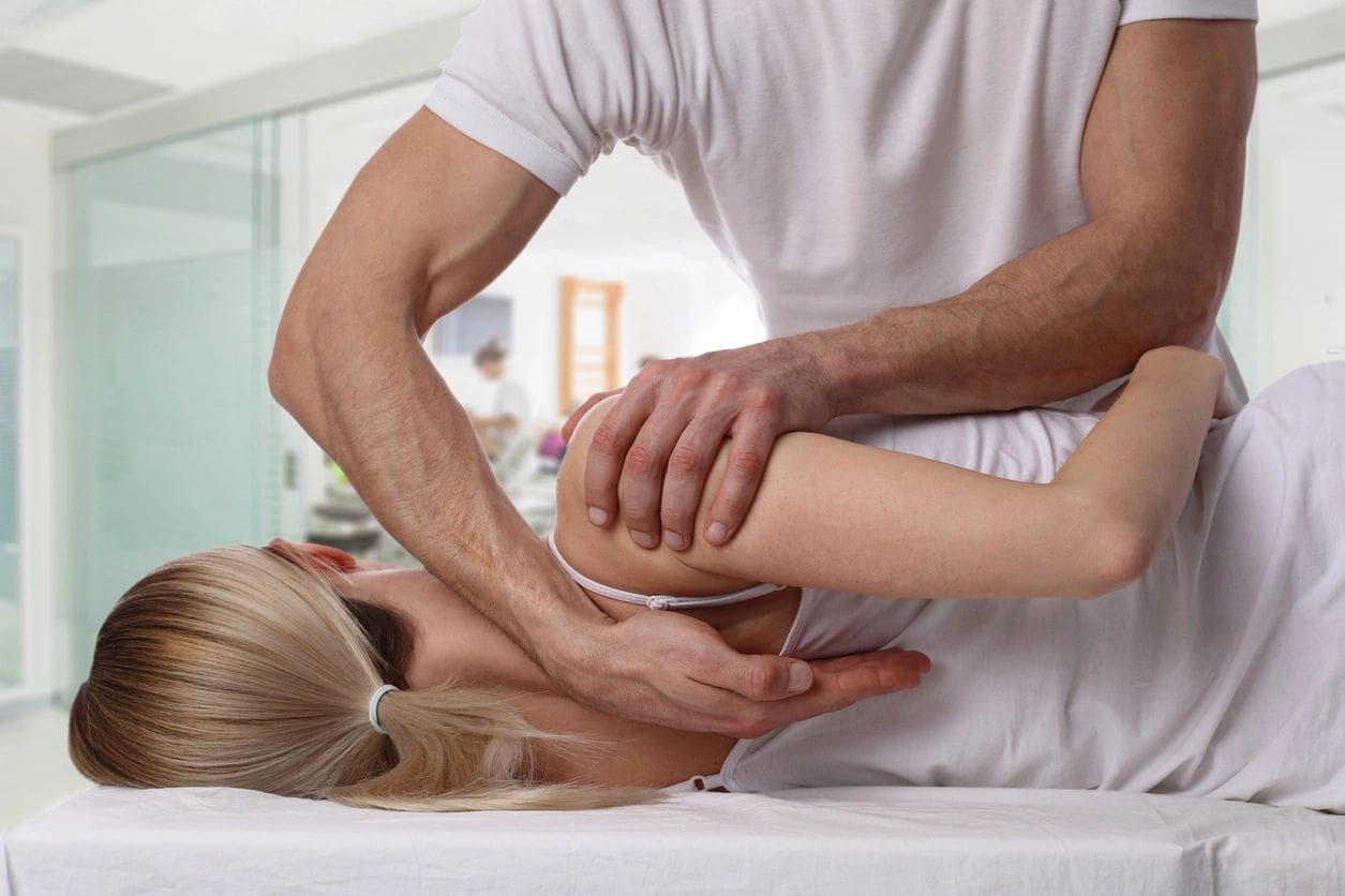 Chiropractor adjusting patient's shoulder on table.