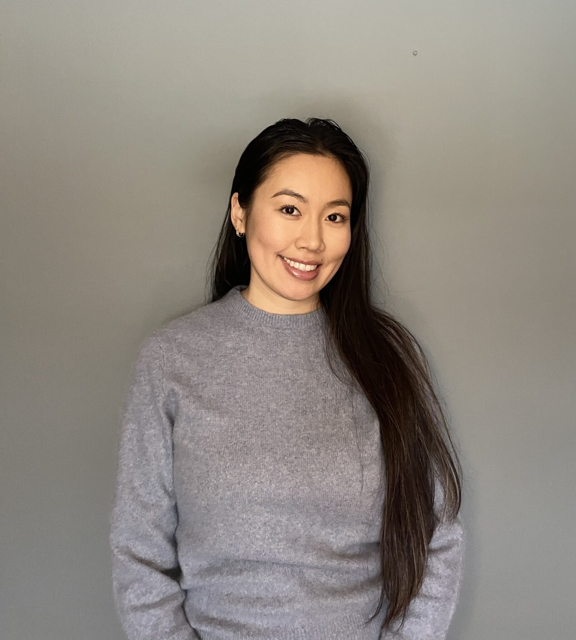 Smiling person in gray sweater, gray background.