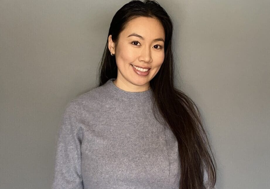 Smiling person in gray sweater, gray background.