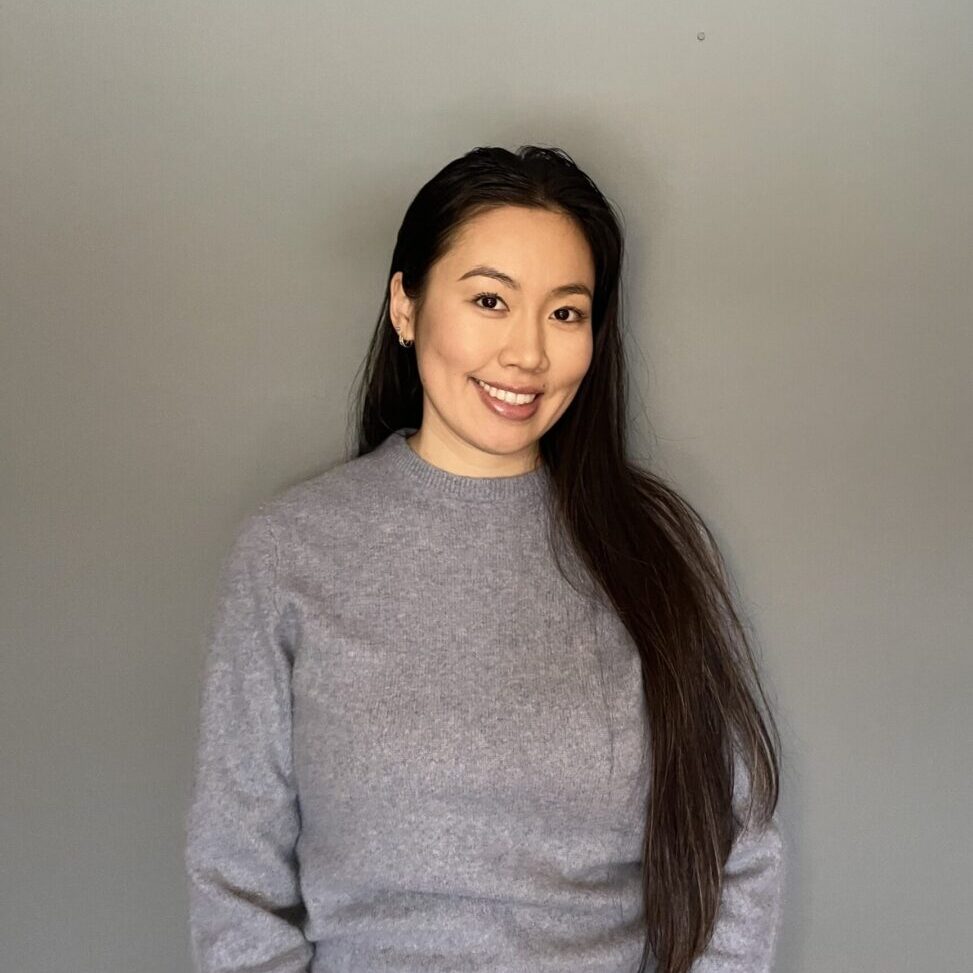 Smiling person in gray sweater, gray background.