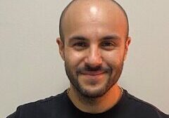 Smiling man in black shirt, neutral background.