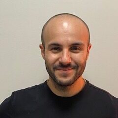 Smiling man in black shirt, neutral background.