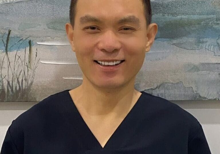 Here's a suggested alt tag: Smiling doctor in dark scrubs.