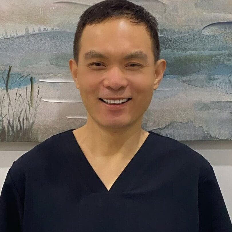 Here's a suggested alt tag: Smiling doctor in dark scrubs.